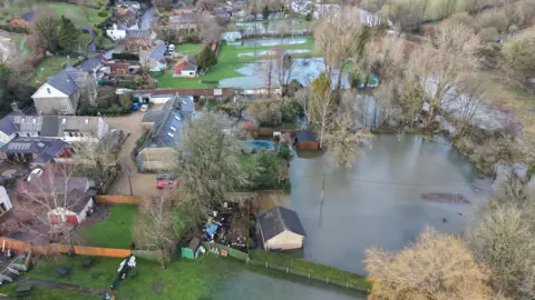 A green field with houses that have been flooded by rain water. 