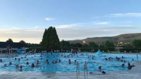 An outdoor swimming pool with dozens of people in it.