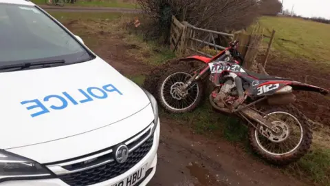 Police vehicle parked next to a muddy off-road bike on the side of a country road in Nottinghamshire