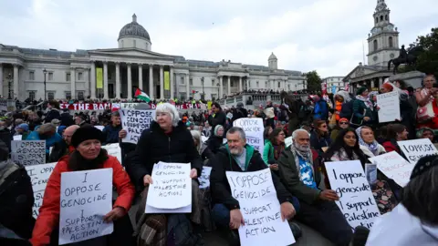 REUTERS/Toby Melville Protesters holding signs saying "I oppose genocide, I support Palestine Action" sit in front of the National Gallery in central London. 