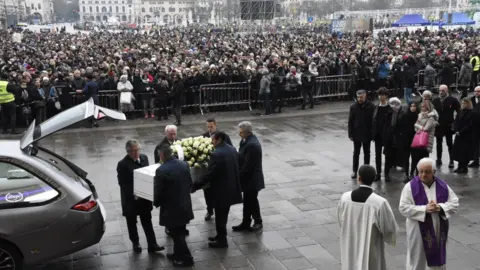 Reuters Men carrying a coffin covered in white roses out of a car boot