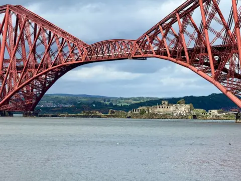 Lorna Donaldson The red Forth rail bridge dominates this picture. There is a grey sky and an island in the distance.
