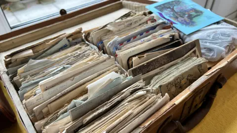 Mike Gould An open suitcase containing many old looking letters. They are neatly arranged in rows. Most are a little tatty around the edges and have yellowed with time. The suitcase is absolutely full of them.