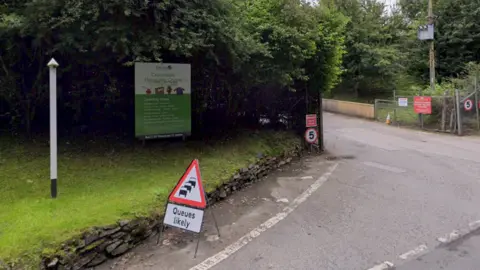 Google The entrance to the Crowndale Recycling Centre with a sign in the road saying queues are likely. There is a sign bearing the name of the centre and further writing which cannot be read in the image. There are also 5mph speed signs either side of the entrance.