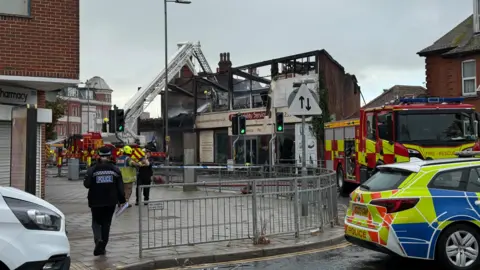 A building is damaged from a fire. Police and fire crew are on the scene and assessing the damage