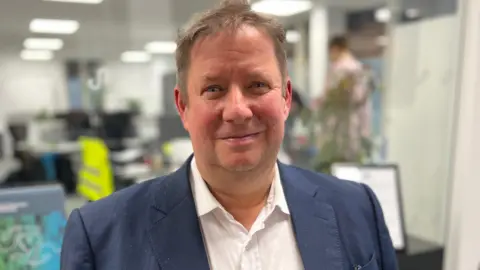 Brent Homan - a man with a blue suit jacket and a white shirt looking at the camera.