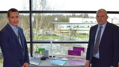 Biocomposites CEO Michael Harris and vice-chancellor of Keele University professor Kevin Shakesheff. Both men are wearing suits. They are standing by a table with promotional materials on it, next to a large window overlooking Keele University's Science and Innovation Park.