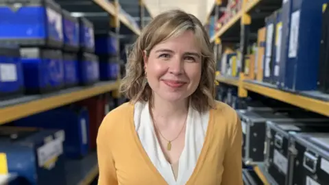 BBC A woman standing in front of storage shelves