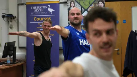 John Fairhall/ BBC Three members of the group performing the "warrior" pose. Their arms are outstretched as they lunge outwards.