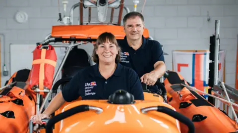 A man and a woman stood in an orange lifeboat.