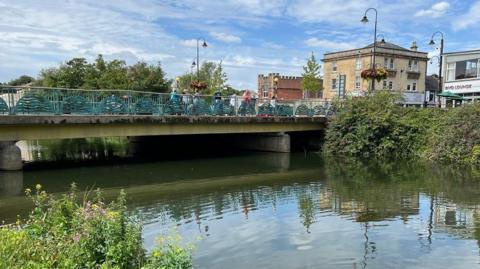 The river on a sunny day in the centre of the town with a bridge over it with people and a swan on the water