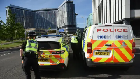 James Chapelard A police car and van parked outside of the Queen Elizabeth with the backs of two police officers standing by the vehicles