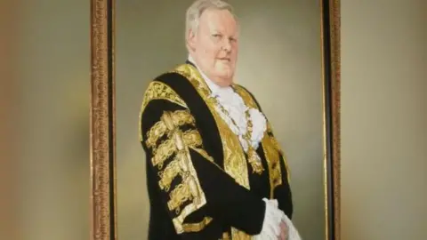 Belfast City Council The portrait of Lord Wallace Browne. He wears a robe with gold ribbons and a gold medallion. 