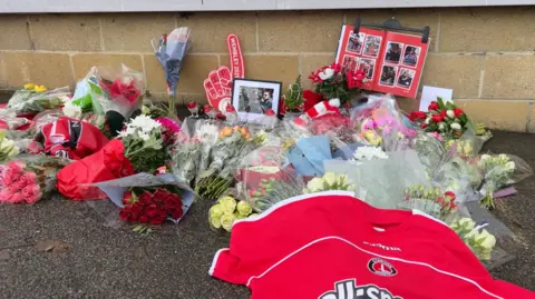 Charlton football shirt, club flags and foam fingers along with flowers on the ground outside the North stand