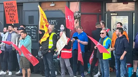 A row of people protesting with banners outside a building