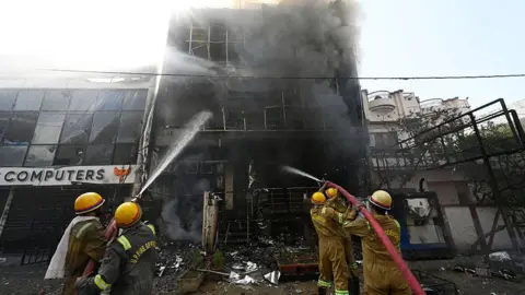 Five firefighters spray water on the burnt building in India's Lucknow. Thick, dark smoke can be seen billowing from the structure.