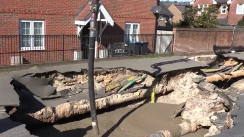 Surrey County Council A black pipe putting foam concrete in a large hole in a street.