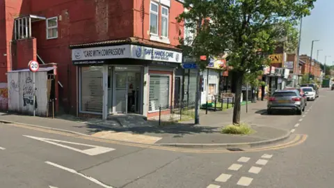 Google streetview of the offices of Safe Hands Care and Support Services on a street corner with parked cars on road.