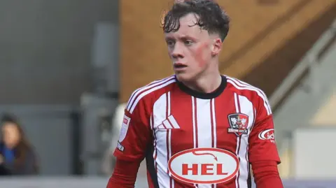 Ethan Brierley in action for Exeter City wearing their red and white striped home jersey