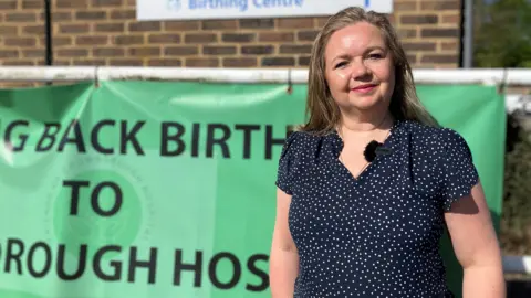 Sam Dixon-French/BBC A woman in a spotted top stands in front of a green campaign sign