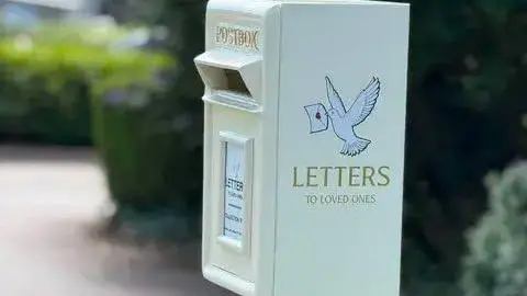 Wadebridge Town Council A white post box with the words "Letters to loved ones" on the side below a dove flying with a letter in its mouth. It has the traditional Post Box writing on the front with a little white plaque on the front.