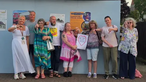 Campaigners stand outside the boarded up bus shelter in Sheringham pointing their thumbs down following the meeting