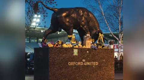 Oxford United The bull statue in front of the Kassam Stadium decorated with flowers and yellow scarfs.