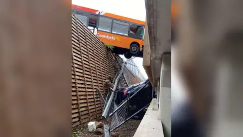 Bus hanging in gap over precipice with crashed car below