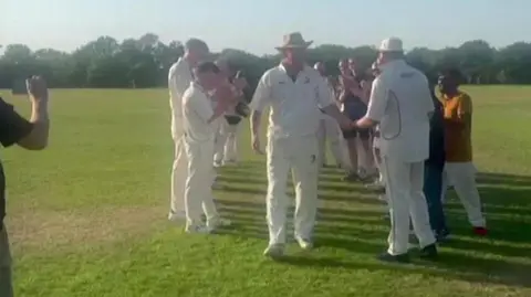 Nic Downes Two lines of cricketers in their whites as Nic Downes, also in his whites, walks between them.