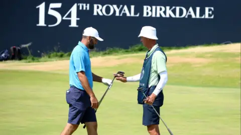 Two men on a golf course in front of a sign reading: '154th Royal Birkdale'.