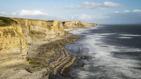 Getty Images Cliffs to the left, with a pebbly beach below and the sea on the right.