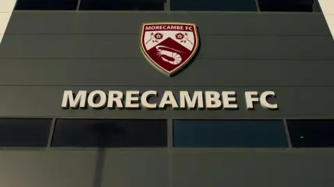 A sign with the Morecambe FC crest outside their Mazuma Stadium home