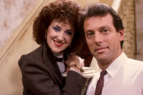 anita dobson and leslie grantham pose around the bannister of the back staircase of the queen vic