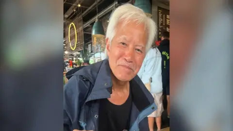 Mr Fong a man with white hair and a moustache wears a navy coat as he sits in a cafe.