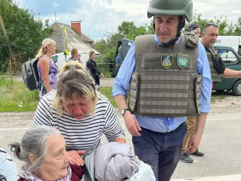 Brooks Newmark Brooks Newmark wearing protective army clothing with two female Ukrainian refugees.