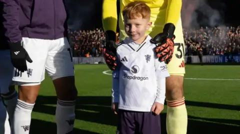 Family photo Image shows Ruari standing with Man Utd goalie Senne Lammens in front of the stands. 
