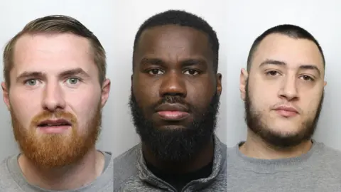 West Yorkshire Police McCorrie has a thick, ginger beard and short hair combed to the side. His mouth is slightly open and he has green eyes. Fogarty has a thick black beard and short curly hair. Dalby has a shaven head and beard along his jaw and upper lip.