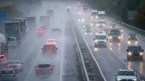PA Media Motorway traffic going away and towards the camera with rain water spraying up.