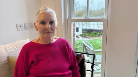 A woman with grey hair sat in a chair. She has a purple top