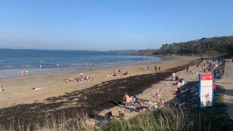 BBC Weather Watcher Happy Snapper People on the sand at Helen's Bay in County Down on 11 April. Beach in the foreground, with blue water in the distance.
