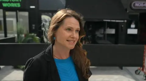 Sarah Chaundler outside the cinema wearing a blue top and black jacket. She has long wavy brown hair. 