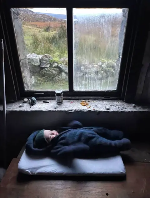 Morag Skelton Hamish lying on a mat in a bothy in front of a window