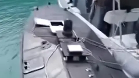 A screenshot showing the discovered naval drone (left) is being towered by a Greek coastguard boat to the port of Vasiliki on the island of Lefkada in the Ionian Sea