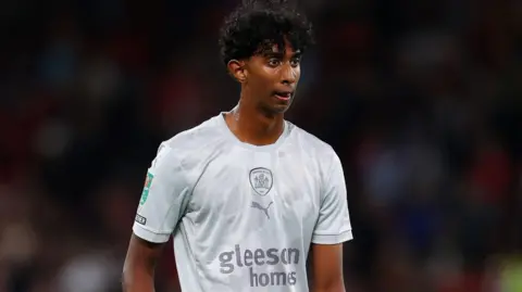 Getty Images Vimal Yoganathan on the pitch in his pearl-grey Barnsley kit. Vimal, sweating, looks focused on the game and a crowd is blurred behind him. 