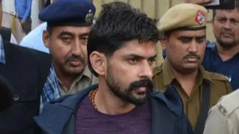 Getty Images Gangster Lawrence Bishnoi is escorted by police personnel before being produced in court on November 13, 2019 in Panchkula, India. Notorious gangsters Lawrence Bishnoi and Sampat Nehra and their aides were produced in a Panchkula district court amid tight security for framing of charges in two criminal cases that took place in 2017.