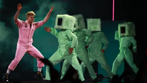 HANNIBAL HANSCHKE/EPA/Shutterstock Look Mum No Computer dances in pink overalls on the stage with four backing dancers dressed in green.