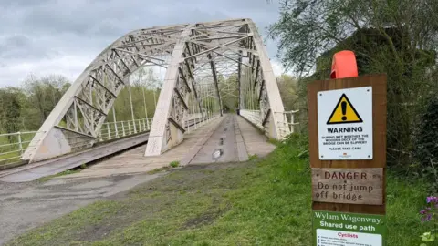 Lawrence O'Donnell A bridge with a span over it is divided into two paths for cycling and walkers. There is a warning sign asking people not to jump off the bridge 