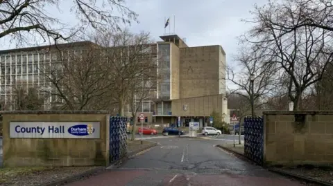 The outside view of County Hall in Durham. It is a large concrete building with a wall of windows on the front.