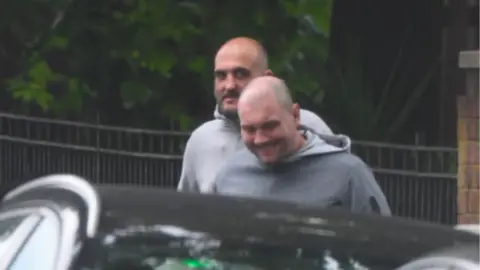 Metropolitan Police Dixon and Loring captured smirking, walking behind a car wearing grey hoodies.