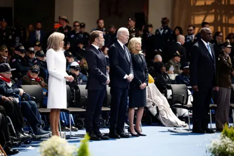 Benoit Tessier/ REUTERS US President Joe Biden (C), US First Lady Jill Biden (R), France's President Emmanuel Macron (2nd L) and French President's wife Brigitte Macron (L) stand to attention during the US ceremony marking the 80th anniversary of the World War II 